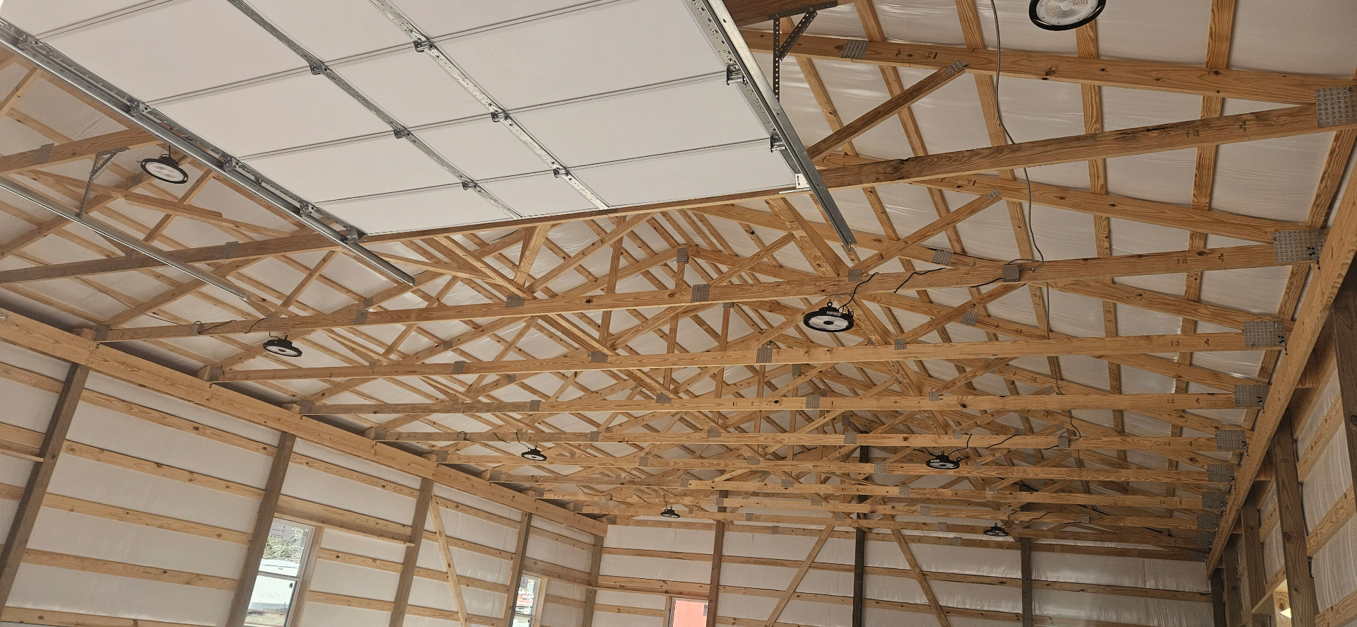 High-bay LED lighting installed in a pole barn ceiling with exposed wood trusses